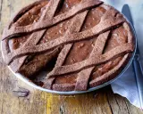 Pastiera al cioccolato con scorze candite, un dolce goloso su un tavolo di legno rustico.
