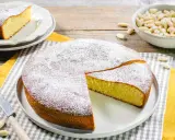 Una deliziosa torta con farina di mandorle, spolverata di zucchero a velo, pronta per essere gustata. Accanto, una ciotola di mandorle intere.