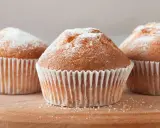 Tre deliziosi muffin senza glutine, spolverati di zucchero a velo, su un tagliere di legno.