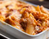 Piatto fumante di pasta pasticciata al forno, con penne ricoperte di sugo e formaggio fuso.