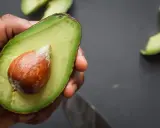 Mano che tiene mezzo avocado maturo con nocciolo. Ecco come si mangia l'avocado: fresco, spalmato o in insalata.