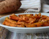 Patate dolci in friggitrice ad aria, tagliate a spicchi e condite con erbe aromatiche, servite in un piatto bianco.