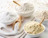 Diverse ciotole mostrano vari tipi di farina, da quella bianca finissima a quelle più grezze e giallastre, pronte per ogni ricetta.