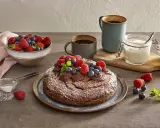 Torta yogurt e cioccolato, cosparsa di zucchero a velo e decorata con frutti di bosco freschi, pronta per essere gustata con un caffè.