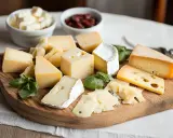 Selezione di formaggi misti su tagliere, con ciotole di formaggio a cubetti e marmellata. Un'idea per gustosi formaggi in gravidanza, con attenzione alla varietà.