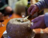 Un uomo serve un formaggio con i vermi, una specialità sarda, con un coltello. Sul tavolo, un bicchiere di vino rosso.