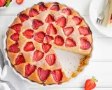 Torta alle fragole dorata, cosparsa di zucchero a velo, con fragole fresche affondate nell'impasto soffice. Una fetta è già stata servita.