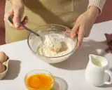 Mani che mescolano farina e burro in una ciotola, con uova, latte e bicarbonato al posto del lievito pronti per la preparazione.