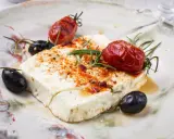 Feta al forno con pomodorini arrostiti, olive nere e rosmarino su un piatto rustico.