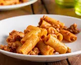 Rigatoni conditi con un ricco ragù di salsiccia alla napoletana, serviti su un piatto bianco.