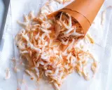 Piccolo cono di carta rovesciato su carta assorbente, con tanti gamberetti surgelati come cucinarli sparsi.