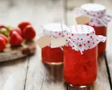 Barattoli di marmellata di fragole fatti in casa, con fragole fresche sullo sfondo.