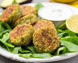 Polpette di spinaci dorate su un letto di spinaci freschi, con una ciotolina di salsa e spicchi di lime.