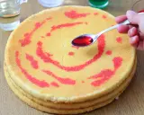 Un cucchiaino di sciroppo rosso viene versato su un pan di spagna decorato con un motivo a spirale. La bagna per pan di spagna renderà la torta più umida e saporita.