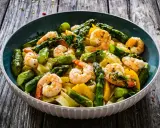 Un piatto invitante di pasta con asparagi e gamberetti, condito con erbe fresche e servito su un tavolo di legno rustico.