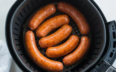 Sette salsicce dorate e succulente cuociono nella friggitrice ad aria, pronte per essere gustate.