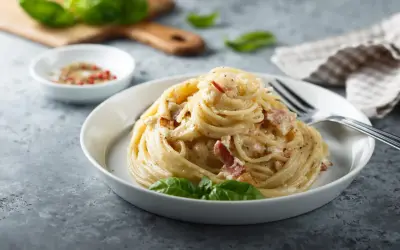 Un piatto di spaghetti alla carbonara, perfetto per la giornata della carbonara, guarnito con basilico fresco.