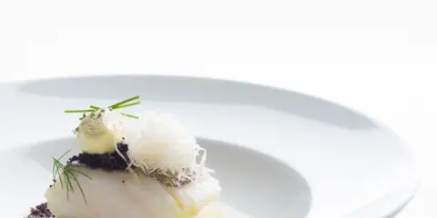 Piatto gourmet con filetto di pesce bianco, crema gialla, erbe aromatiche e fili croccanti. Un'interpretazione moderna che evoca la differenza tra baccalà e stoccafisso.