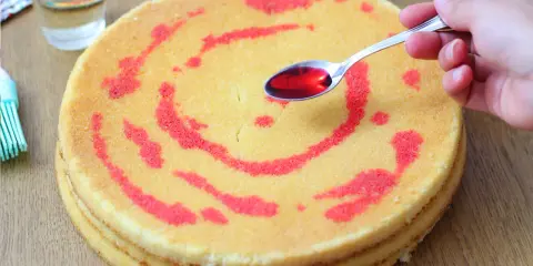 Un cucchiaino di sciroppo rosso viene versato su un pan di spagna decorato con un motivo a spirale. La bagna per pan di spagna renderà la torta più umida e saporita.