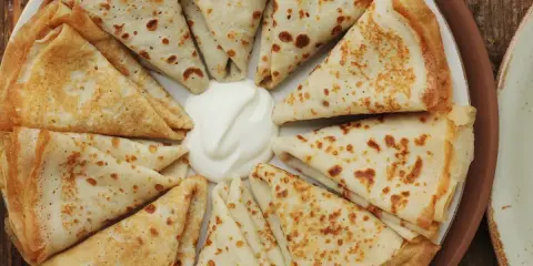 Piatto di crespelle ripiene, piegate a spicchi, con una generosa porzione di panna acida al centro.