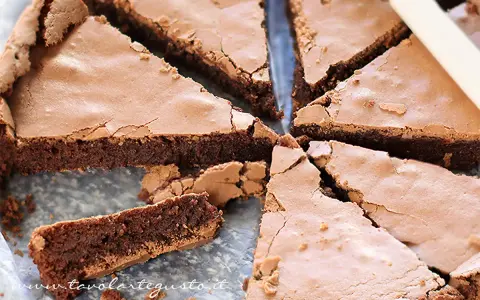 Una deliziosa torta tenerina al cioccolato, tagliata a fette triangolari, mostra la sua crosta croccante e il cuore morbido.