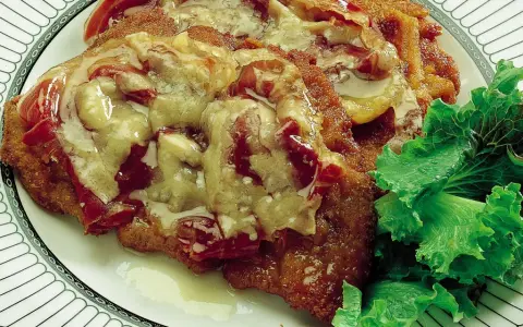 Cotoletta alla bolognese ricoperta di sugo e formaggio fuso, servita con insalata fresca su un piatto decorato.