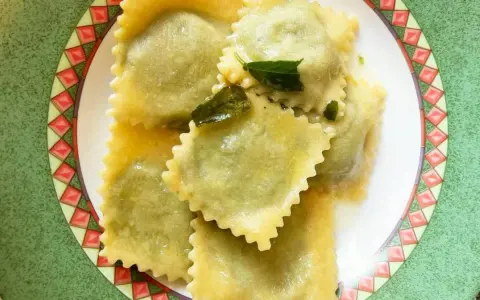 Ravioli ricotta e spinaci conditi con burro fuso e salvia, serviti su un piatto decorato.