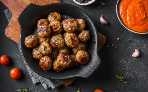 Polpette dorate e succulente, appena sfornate dalla friggitrice ad aria, pronte per essere gustate con salsa e pomodorini freschi.