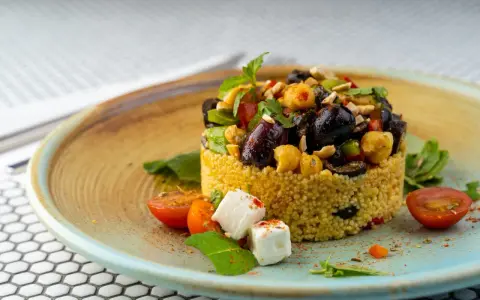 Cous cous condito con olive, ceci, pomodorini e feta. Un'idea gustosa su come condire il cous cous per un piatto colorato e saporito.