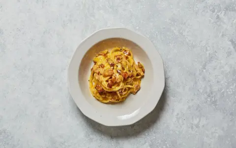 Un piatto di spaghetti alla carbonara, con il suo guanciale croccante e la crema d'uovo e pecorino, pronto per essere gustato.