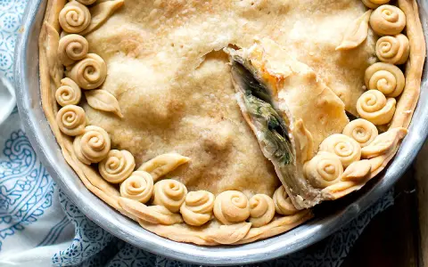 Torta salata con carciofi, decorata con rose di pasta frolla e foglie, pronta per essere gustata.