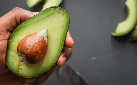 Mano che tiene mezzo avocado maturo con nocciolo. Ecco come si mangia l'avocado: fresco, spalmato o in insalata.