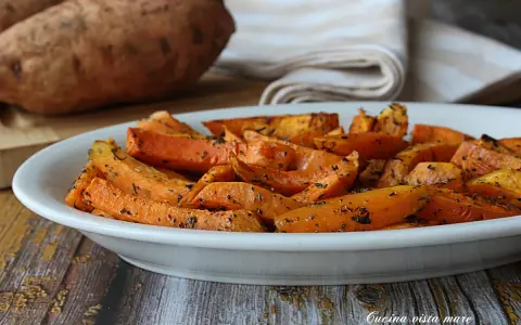 Patate dolci in friggitrice ad aria, tagliate a spicchi e condite con erbe aromatiche, servite in un piatto bianco.