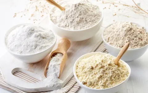 Diverse ciotole mostrano vari tipi di farina, da quella bianca finissima a quelle più grezze e giallastre, pronte per ogni ricetta.