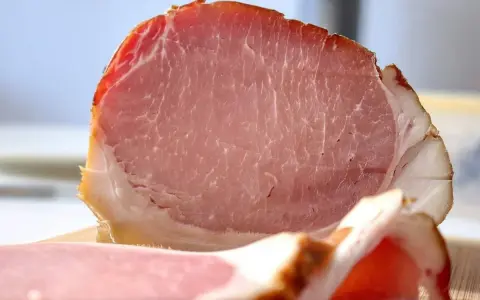 Fetta di prosciutto cotto, un insaccato rosa con striature di grasso bianco e un bordo dorato.