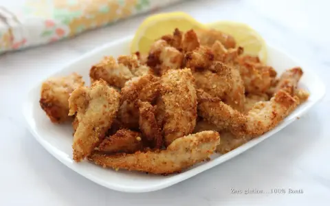 Straccetti di pollo croccanti in friggitrice ad aria, serviti con spicchi di limone.