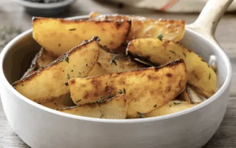 Patate in padella dorate e croccanti, condite con erbe aromatiche, servite in una ciotola bianca.