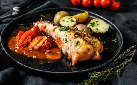 Un succulento piatto di coda di rospo cotta al forno, servita con pomodori e patate novelle.