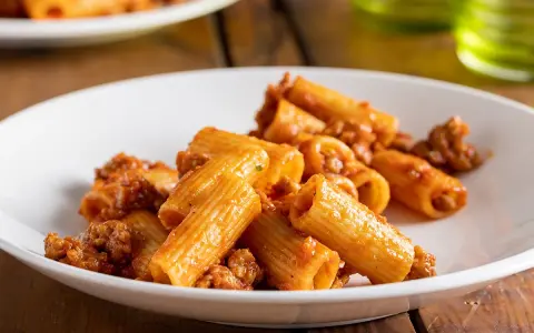 Rigatoni conditi con un ricco ragù di salsiccia alla napoletana, serviti su un piatto bianco.