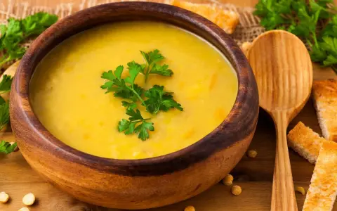 Vellutata di ceci cremosa in ciotola di legno, guarnita con prezzemolo fresco e accompagnata da crostini dorati.