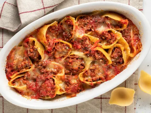 Conchiglioni ripieni al forno, un piatto invitante con pasta ripiena di carne, salsa di pomodoro e formaggio fuso, pronto per essere gustato.