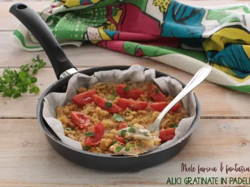 Alici gratinate in padella, un piatto semplice e gustoso con pomodorini e pangrattato, pronto per essere assaporato.