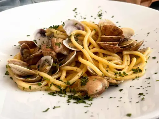 Spaghetti con lupini di mare, un piatto di pasta fresca condita con molluschi e prezzemolo tritato, servito su un piatto bianco.
