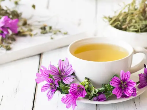 Una tazza di tisana alla malva, decorata con fiori viola, pronta a donare i suoi benefici.
