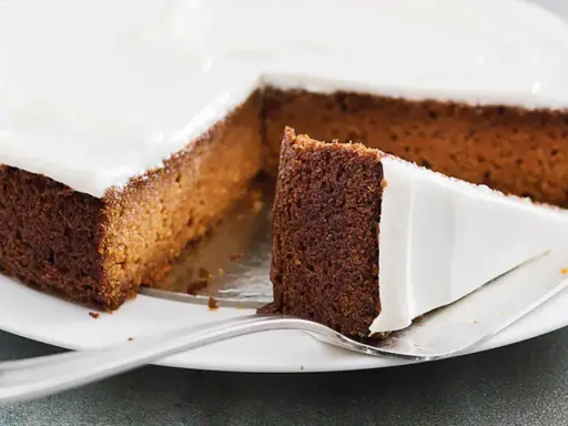 Una fetta di torta di carote e yogurt, soffice e ricoperta di glassa bianca, pronta per essere gustata.