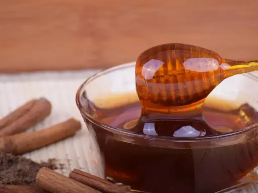 Miele di castagno, ricco di proprietà benefiche, gocciola da un cucchiaio in una ciotola. Cannella e polvere scura completano la scena.