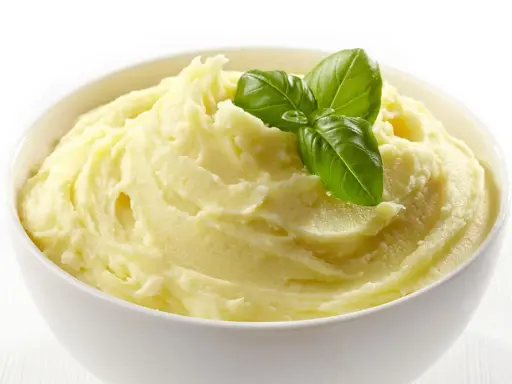 Una ciotola bianca piena di soffice crema di patate, guarnita con foglie di basilico fresco.