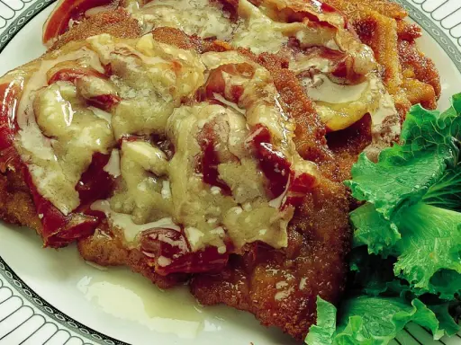 Cotoletta alla bolognese ricoperta di sugo e formaggio fuso, servita con insalata fresca su un piatto decorato.