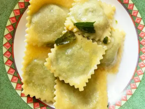 Ravioli ricotta e spinaci conditi con burro fuso e salvia, serviti su un piatto decorato.