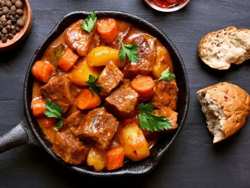 Un saporito capretto in umido, ricco di patate e carote, servito in una padella di ghisa, accompagnato da pane rustico.
